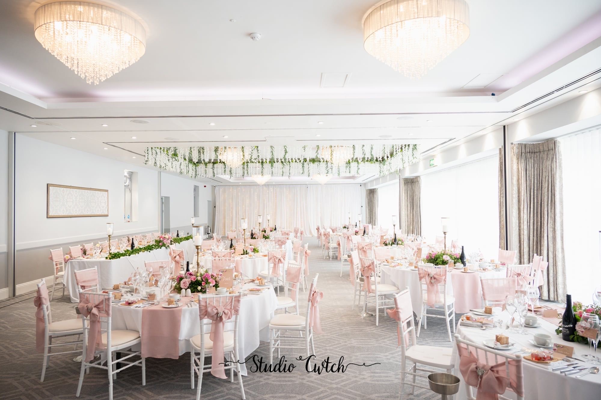 Blush pink ballroom reception with hanging greenery installation and floral top table