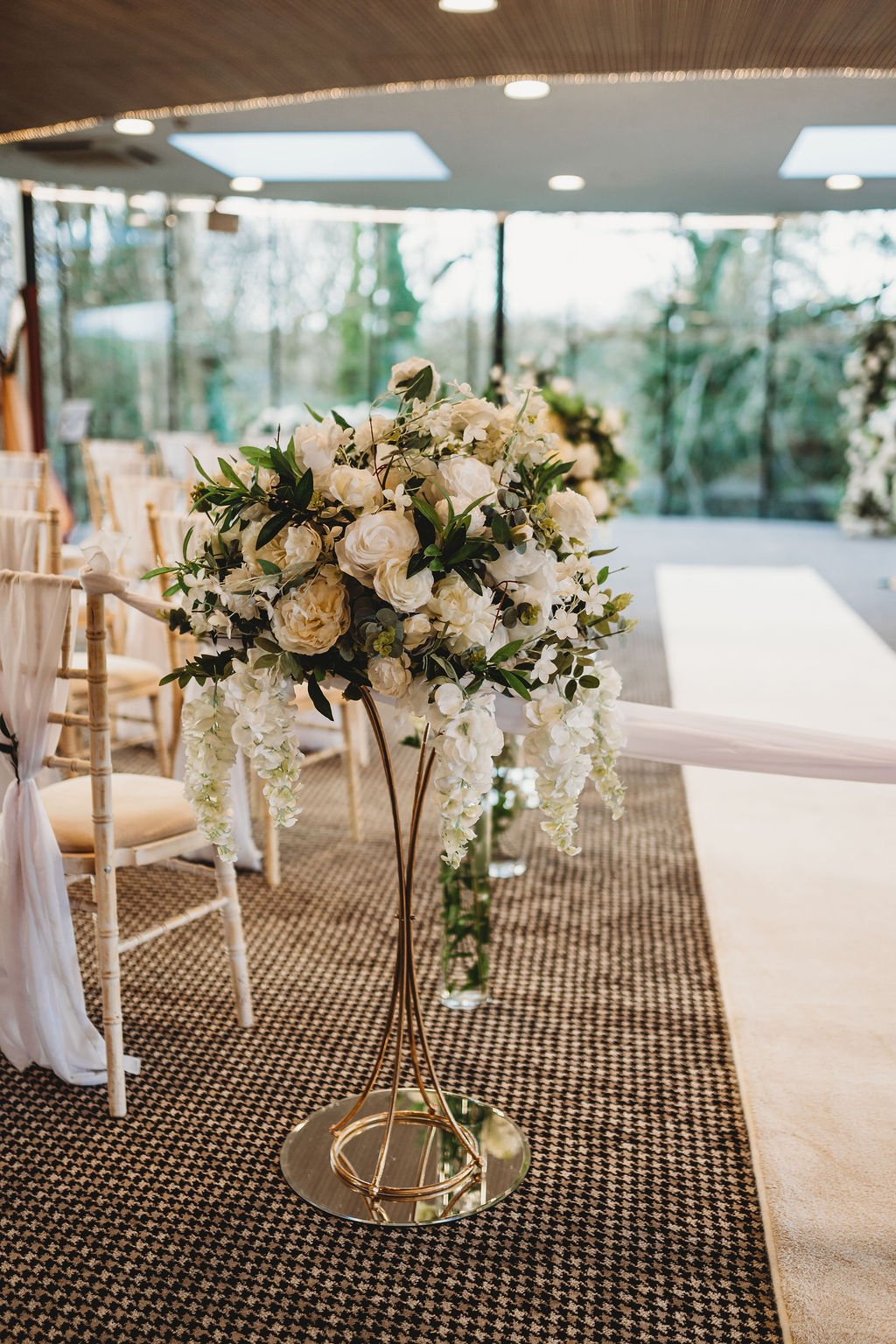 Tall gold stand centrepiece with ivory roses and cascading wisteria beside the ceremony aisle