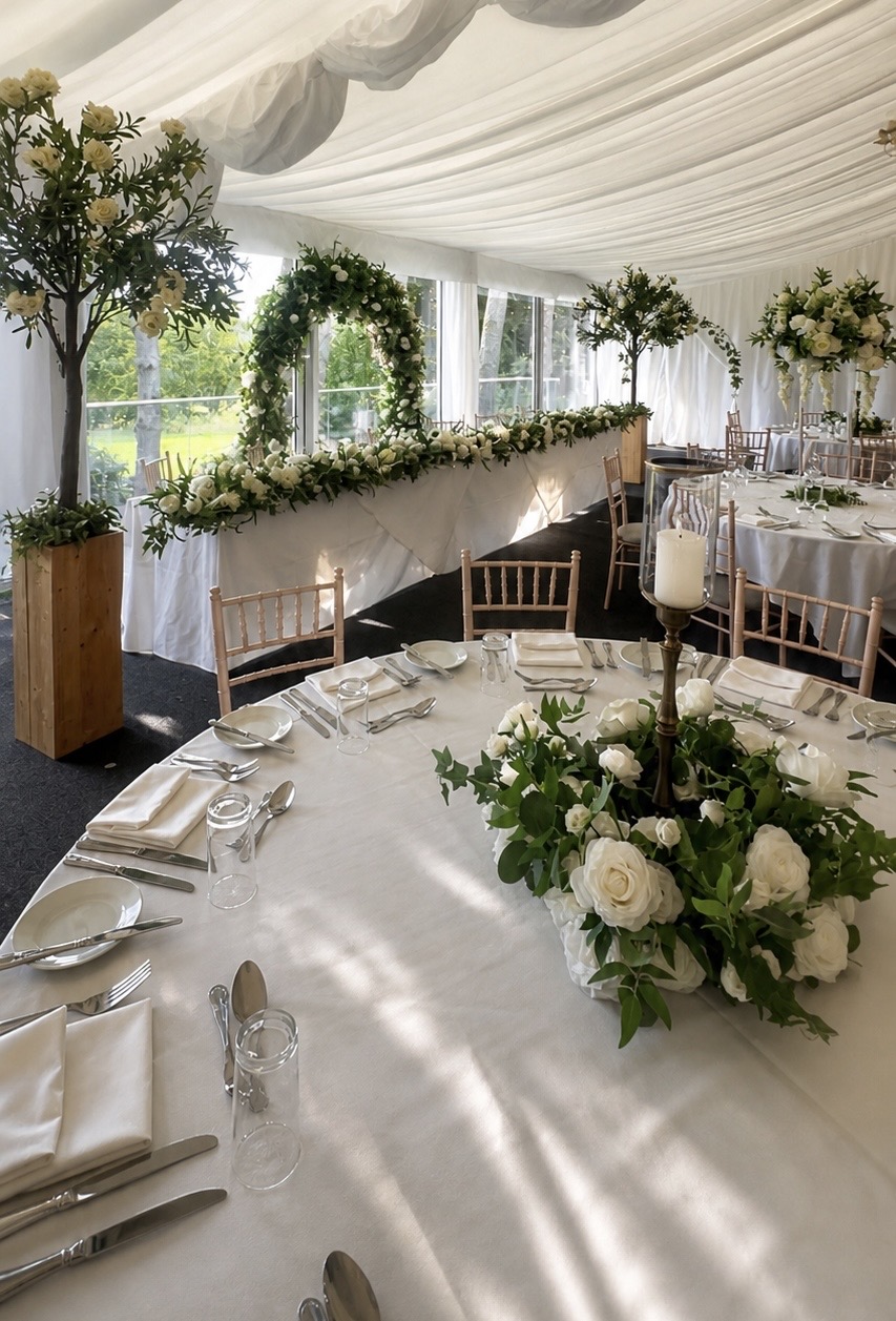 Reception marquee with white floral styling, greenery arches and elegant table details