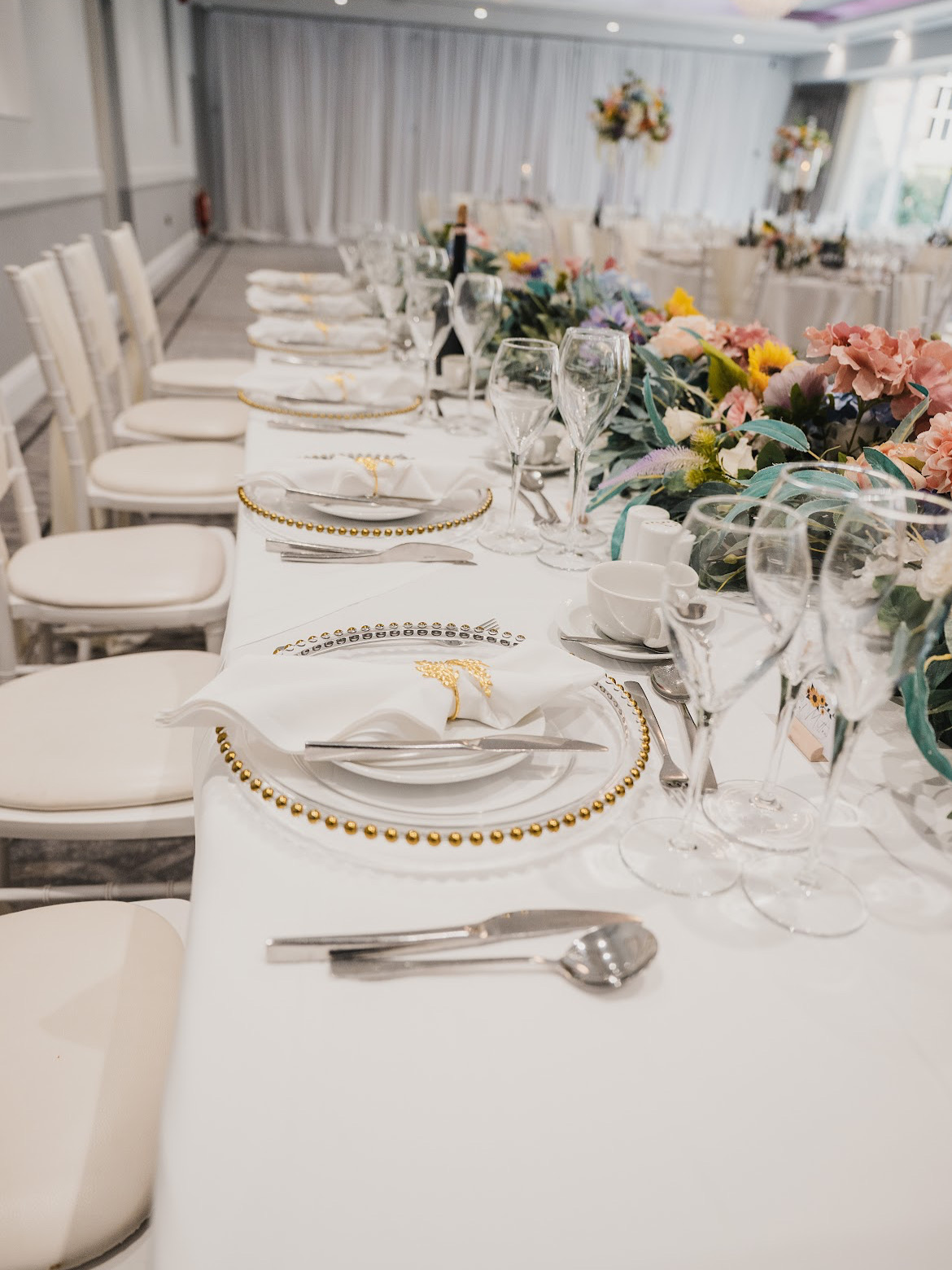 Long banquet table with gold-beaded chargers and a colourful pastel floral runner