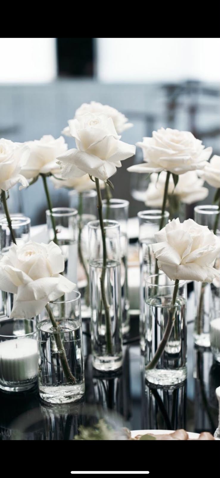 White roses in single-stem glass vases on mirror
