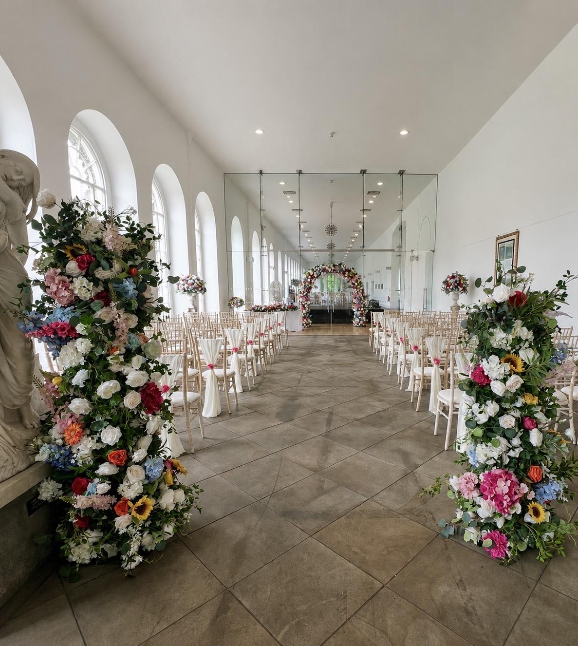 Ceremony aisle framed with colourful floral pillars and mirrored backdrop
